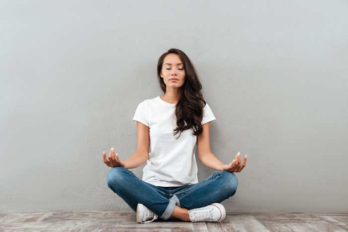 Beautiful young asian woman sitting in yoga position and meditating isolated over gray background