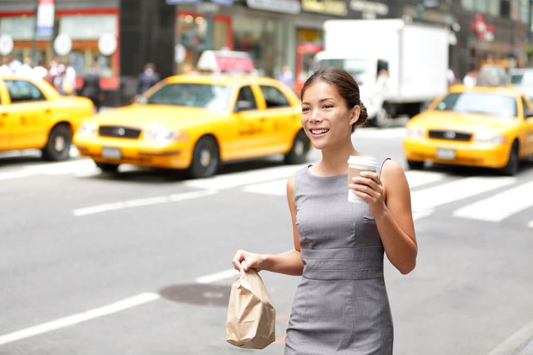 Business woman in New York City candid and real. Businesswoman in Manhattan walking in dress suit holding doggy bag drinking coffee smiling happy. Young multiracial Asian Caucasian professional female