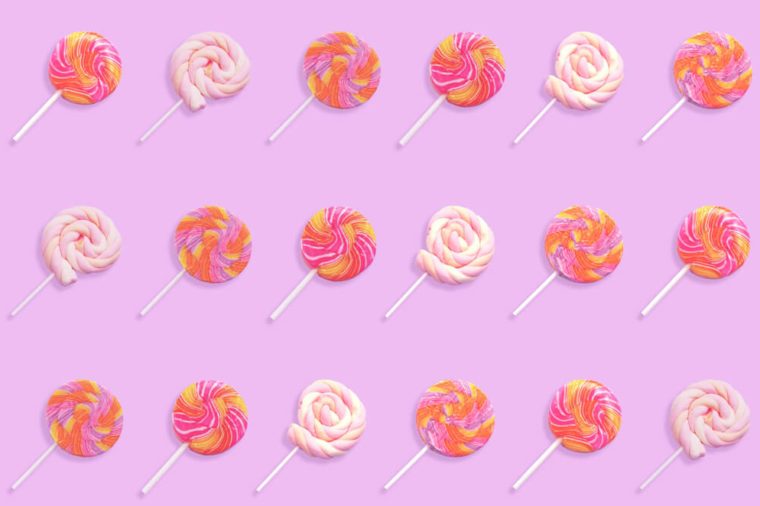 Pattern of colorful lollipop candy with stick isolated on violet background. Flat lay. 