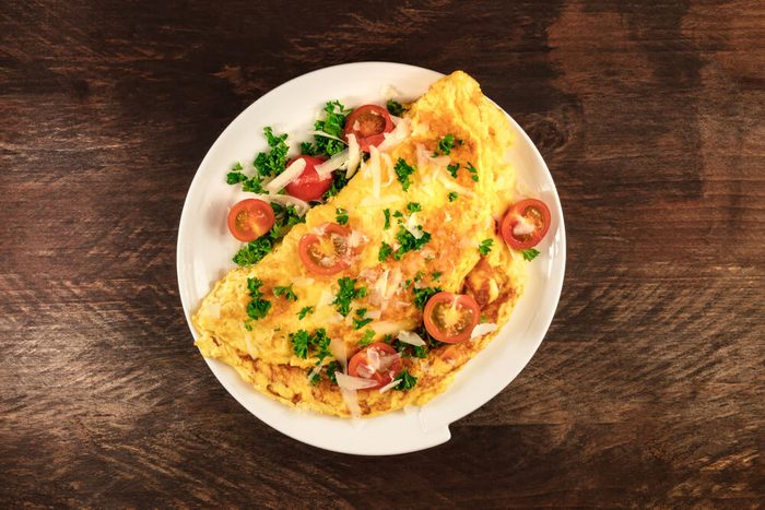 A photo of an omelette with cherry tomatoes, parsley. and grated cheese, shot from above on a rustic wooden texture with a place for text