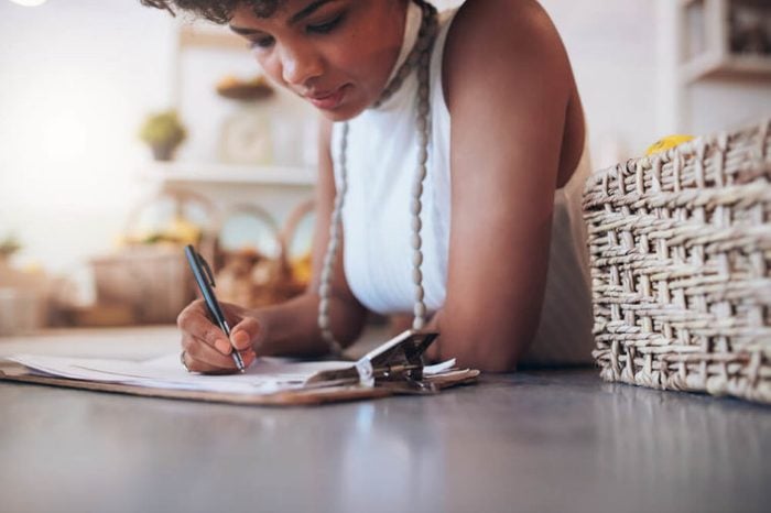 Cropped image of young african woman working in a juice bar. Female standing behind the counter and writing notes. Calculating a customer bill.