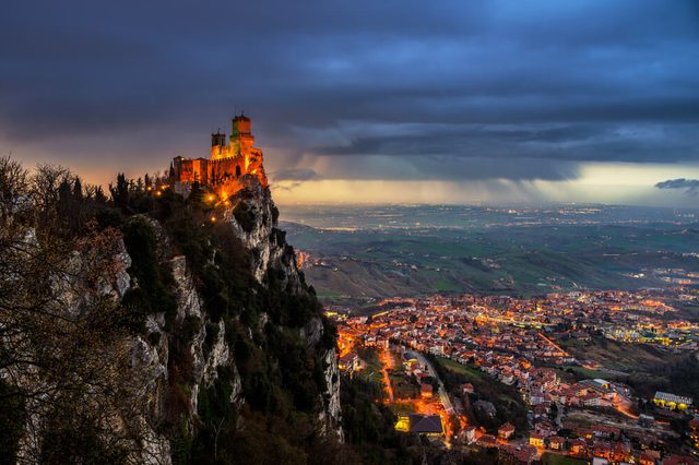 San Marino fortress of Guaita on Mount Titano at sunset. Heavy raining clouds with aerial view at the city. Car traffic lights and illumination