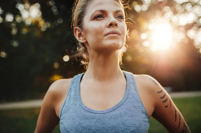 Close up portrait of fit young woman in sportswear standing outdoors and looking away. Confident fitness model in park.