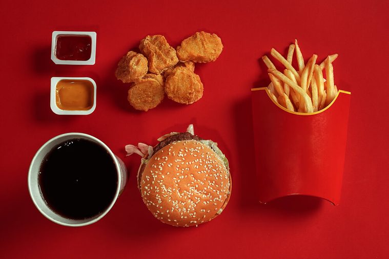 Concept of mock up burger, potatoes, sauce, chicken nuggets and drink on red background. Copy space for text and logo.