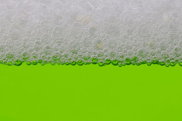 Closeup of a green liquid with a line of bubbles at the top.