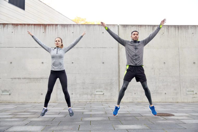 fitness, sport, people, exercising and lifestyle concept - happy man and woman doing jumping jack or star jump exercise outdoors