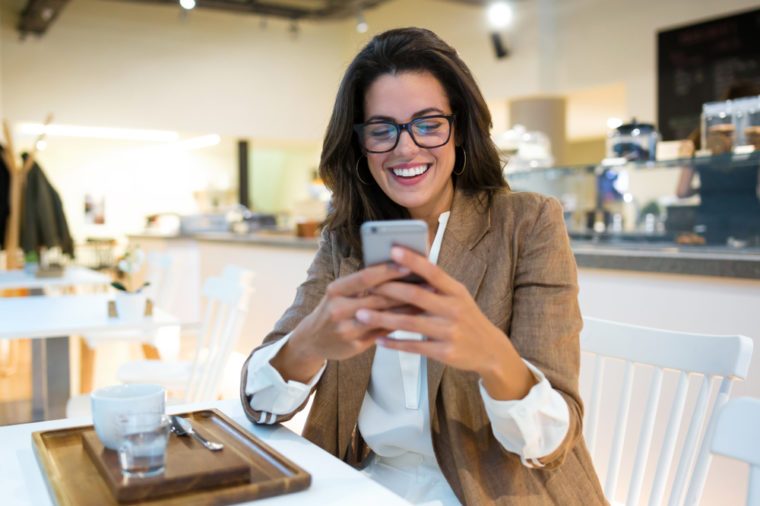 Shot of laughing young businesswoman texting with her mobile phone in the coffee shop.