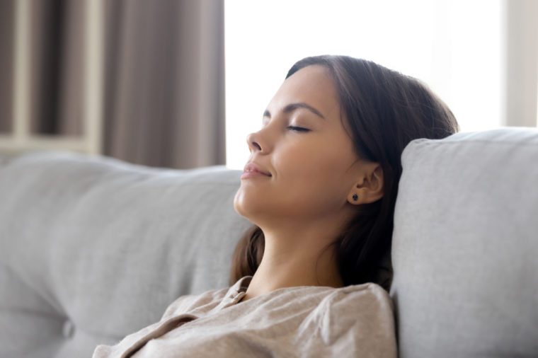 Serene calm woman relaxing leaning on comfortable couch having nap breathing fresh air dreaming, lazy relaxed girl lounging with eyes closed on sofa enjoy stress free peaceful day wellbeing at home