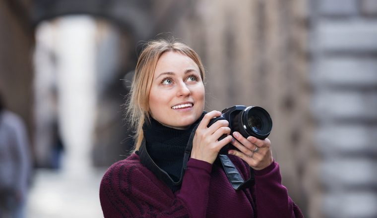 Happy smiling girl taking picture with camera in the town