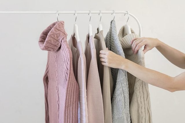 Woman choosing pastel warm cozy sweaters on hangers