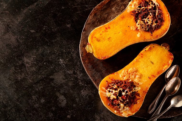 Halved roasted butternut squash with spicy filling viewed overhead on a rustic flat metal plate with spoons and copyspace for healthy seasonal autumn cuisine