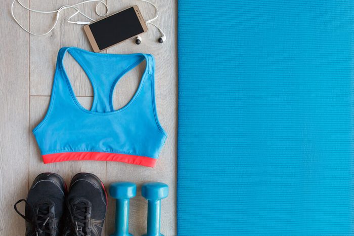 View from above of Fitness and sport equipment. Healthy lifestyle concept. Sneakers, sportswear, dumbbells, cell phone and headphones on blue mat wooden floor background, top view
