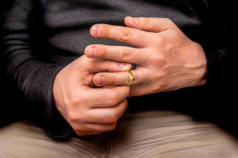 Disappointed man is taking off his wedding ring isolated on black - divorce concept