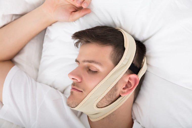Young Handsome Man Sleeping With Anti Snoring Chin Strap On Head At Home