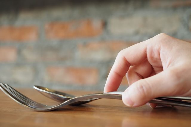 Hand holding fork and spoon over the dinner table