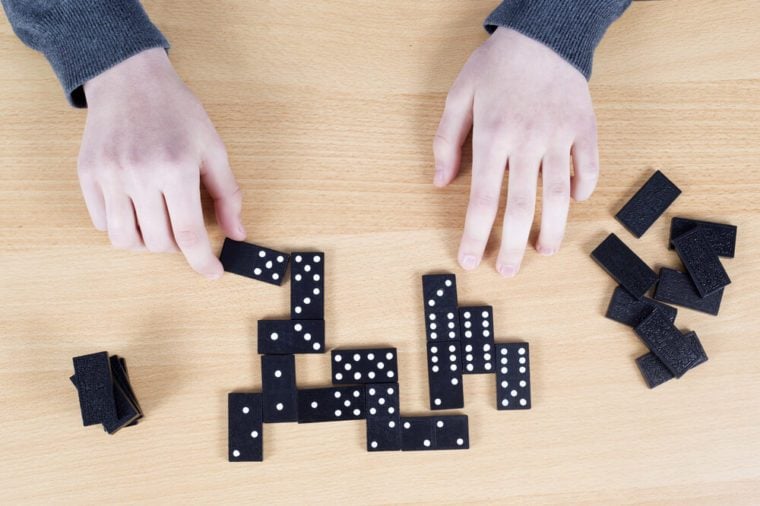 Top View Of Female Hands And Black Dominoes On Wooden Board