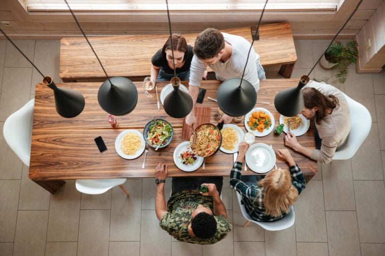Top view of group of people having dinner together while sitting at the rustic wooden table at home