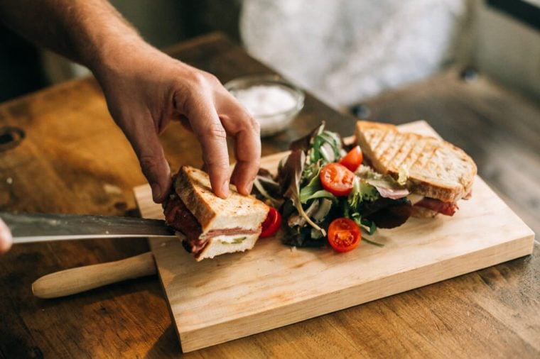 Man prepares lunch, serves grilled bread sandwich snack on top of wooden cutting board, with side of green salad, healthy alternative to burgers and grease