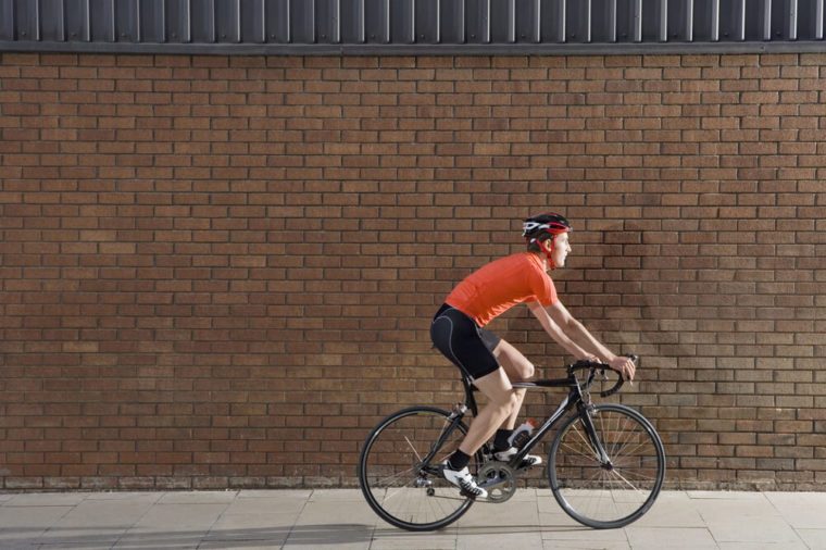 Full length side view of a young man cycling past brick wall