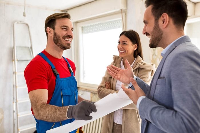 Young smiling couple and handyman talking about details of renovations home