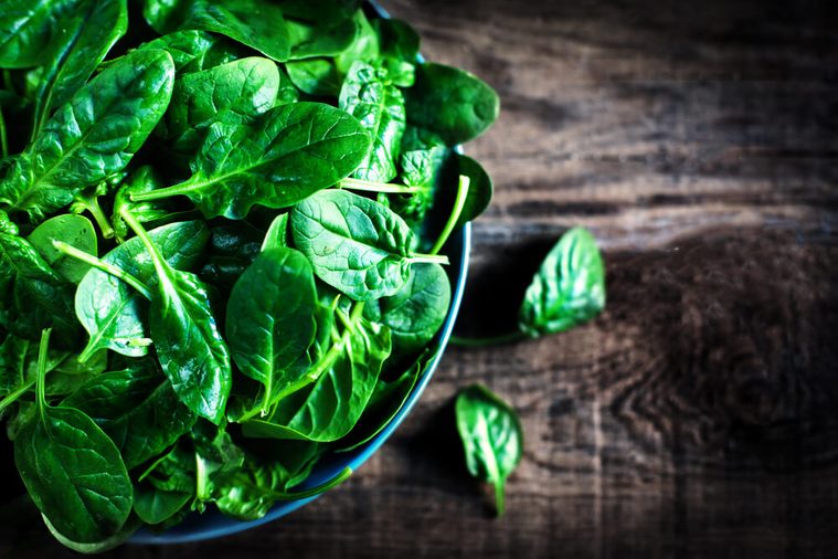 Fresh green baby spinach leaves in a bowl on a rustic wooden table close up