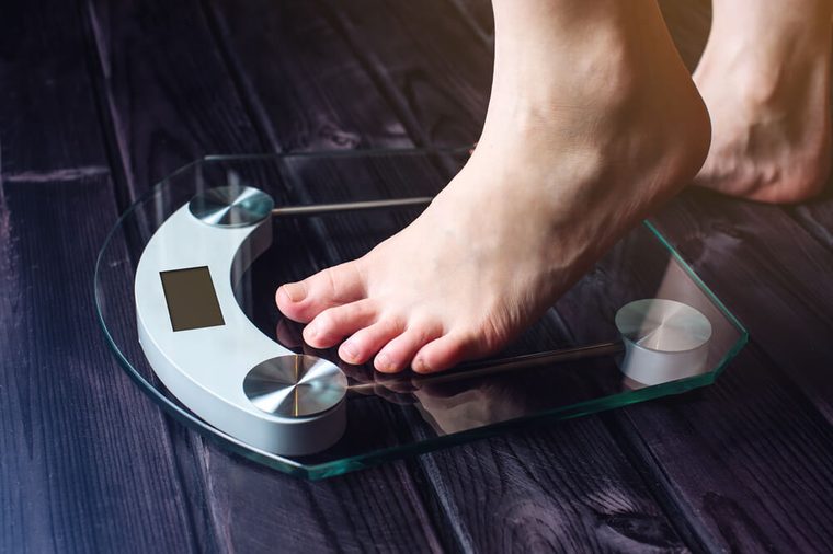 Female feet standing on electronic scales for weight control on wooden background. The concept of slimming and weight loss
