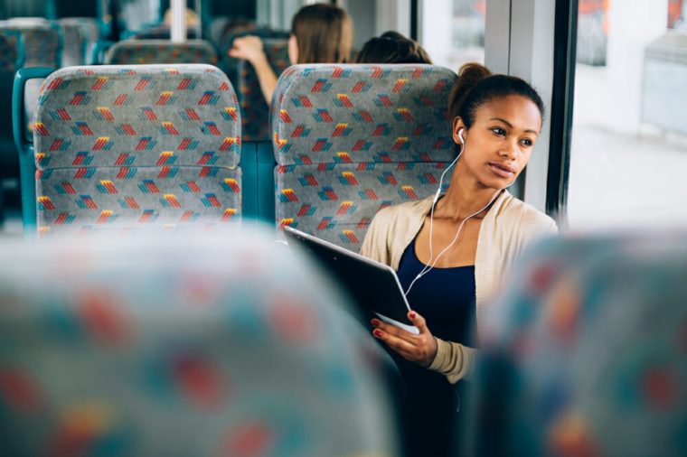 Young woman listening to music on train using tablet computer