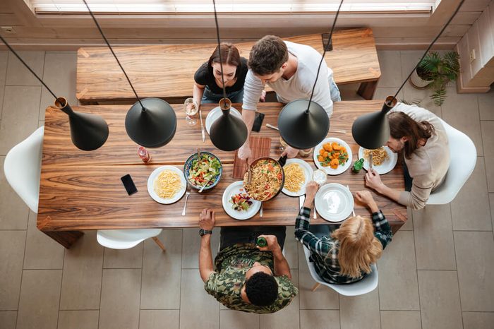 Top view of group of people having dinner together while sitting at the rustic wooden table at home