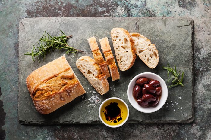 Fresh ciabatta with olive oil and olives on stone slate background