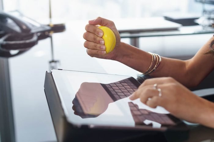 Office worker typing email on tablet computer. The woman feels stressed and nervous, holds an antistress yellow ball in her hand