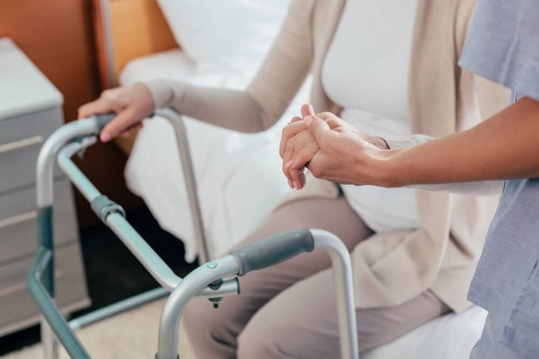 cropped shot of senior patient with walker and nurse holding hands 