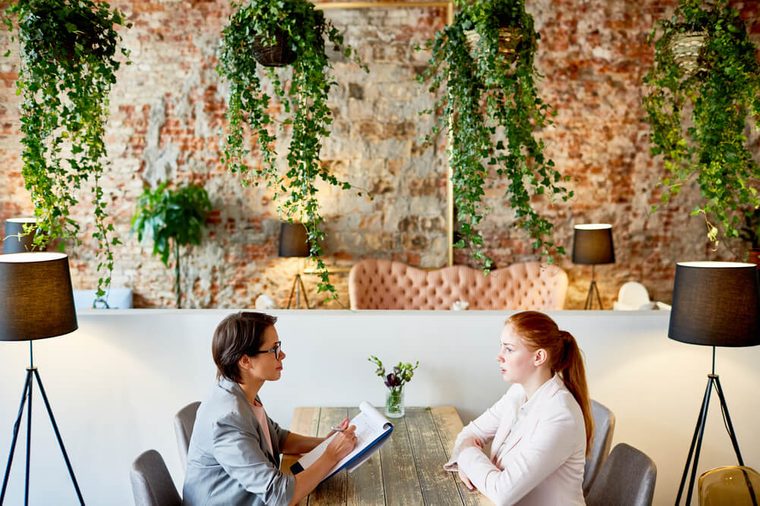 Profile view of female HR manager conducting interview with young red-haired applicant for position while sitting at fashionable restaurant with creative design