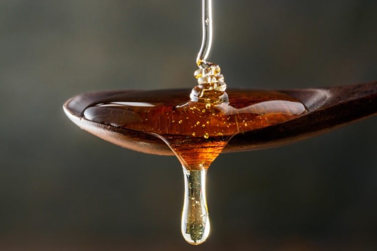 Honey pouring on wooden spoon and dripping from spoon. Dark background. Extreme close up