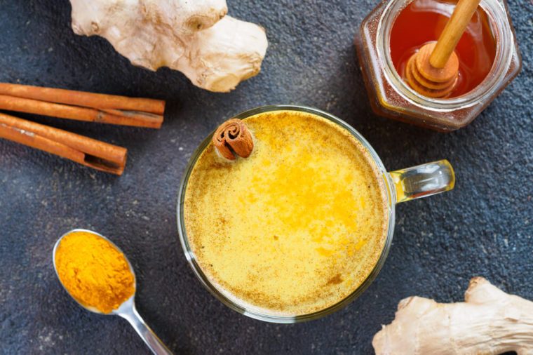 Healthy drink golden turmeric latte in glass cup.Gold milk with turmeric,ginger root,cinnamon sticks,turmeric powder and honey on black background.Detox turmeric tea and ingredients.Top view flat-lay.