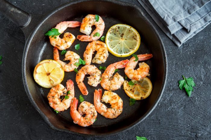 Roasted shrimps with lemon, garlic and herbs. Seafood, shelfish. Shrimps Prawns grilled with spices, garlic and lemon on black stone background, copy space. Shrimps prawns on cast iron pan.