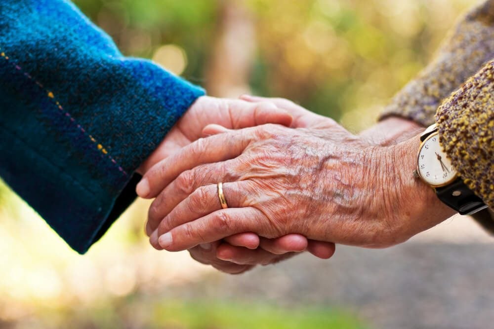 Couple de personnes âgées se tenant la main à l'extérieur.