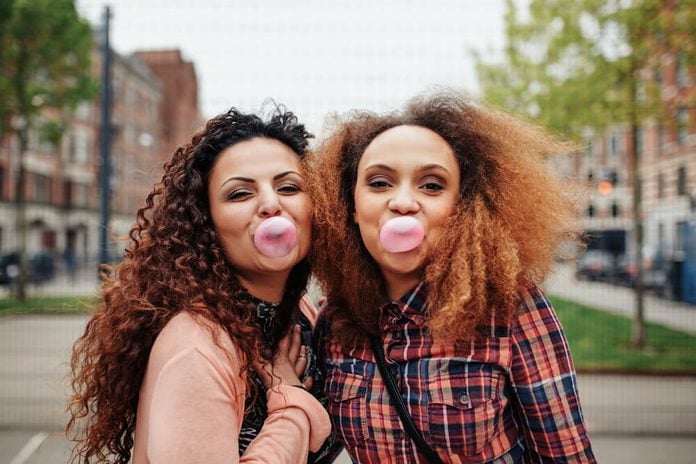 Happy young women blowing bubble gum. Best friends chewing bubble gum, outdoors.