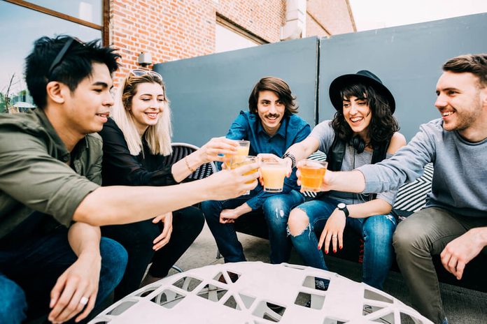 Group of young multiethnic friends sitting in a bar toasting, talking to each other, having fun - happy hour, friendship, relax concept