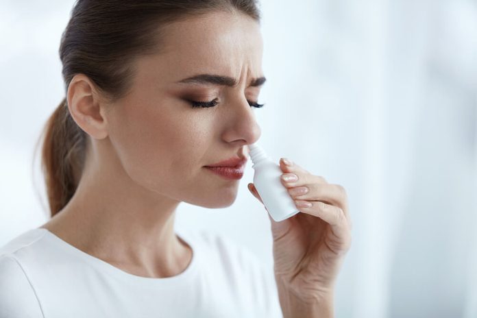 Illness And Sickness. Closeup Of Beautiful Woman Feeling Sick Dripping Nasal Drops In Blocked Nose. Portrait Female Sprays Cold And Sinus Medicine In Runny Nose. Sinusitis treatment. High Resolution