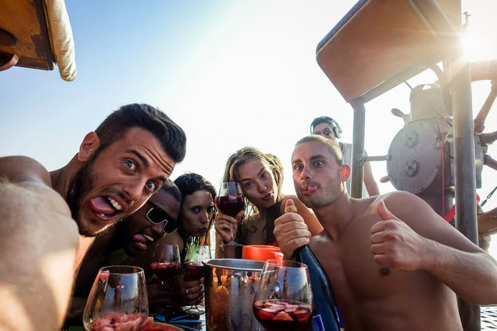 Happy friends taking selfie photo with mobile phone camera in boat party - Young people having fun in ibiza drinking champagne sangria - Summer vacation concept - Warm filter