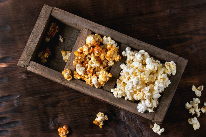 Prepared salted and caramelized sweet popcorn in old wood three sectioned box over dark textured wooden background. Top view. With space for text