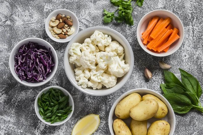 Variety of fresh vegetables in bowls - potatoes, red and cauliflower cabbage, spinach, green onions, carrots, nuts, olive oil, cilantro. Raw ingredients. Vegan table. Top view