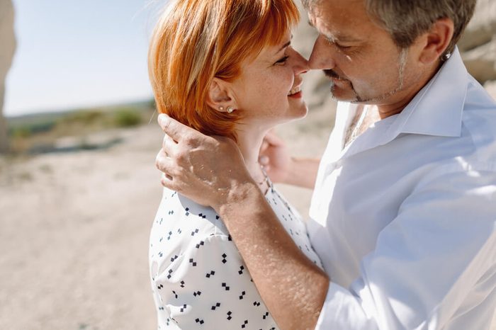 couple middle-age years in white shirts walks between sandstone rocks. holding hands, hugging, kissing. happiness love. standing against the sky. close-up portraits gentle