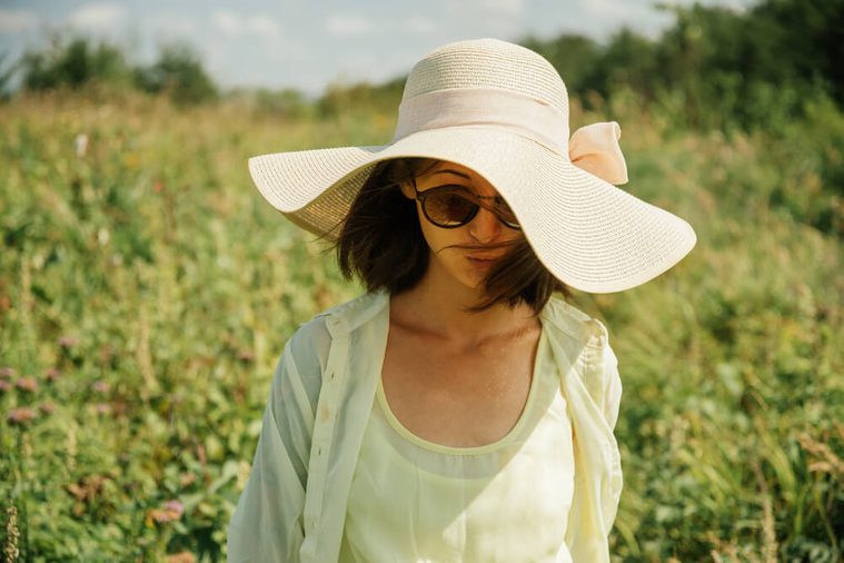 Beautiful woman in sunglasses and hat with wide brim on nature in summer