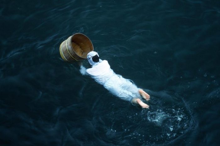 Traditional female pearl diver swimming in the water with wooden barrel for collecting oysters at the Mikimoto Pearl Farm in Mie Prefecture in Kansai Region. JAPAN