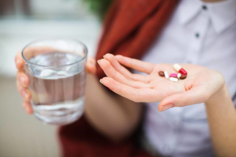 Woman hand with pills medicine tablets and glass of water 