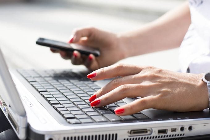 Hands of a businesswoman typing on a computer keyboard and holding phone in the other hand