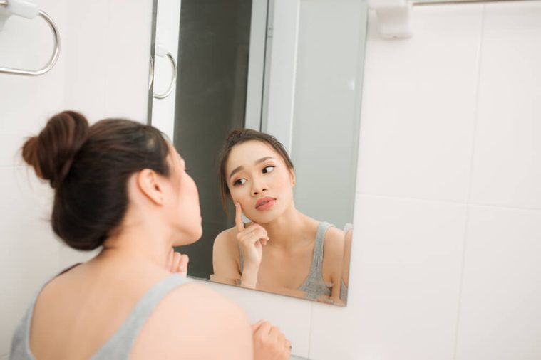 Asian woman holding a mirror, touch and worrying about her face