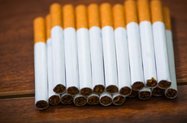 Stack of many cigarettes placed on wooden surface, as seen from above, artistic anti smoking concept
