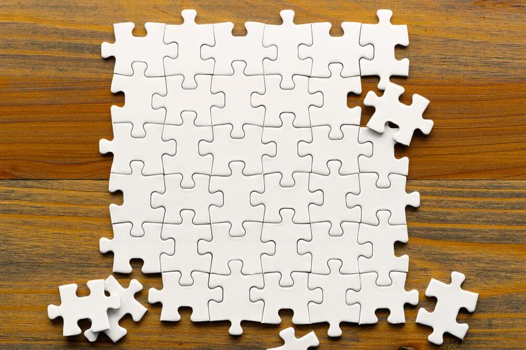 White puzzle pieces on wood background. Partially completed square shaped puzzle pieces.